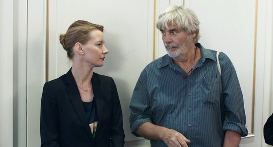 Een vrouw met een zwart pak en een man met een blauw gestreept overhemd praten met elkaar.