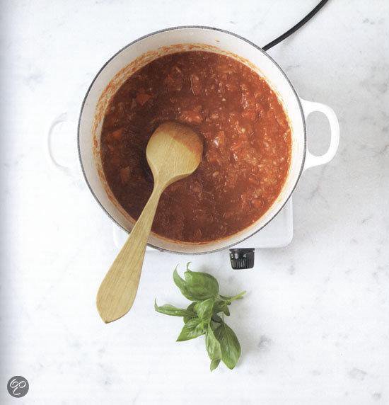 Tomatensaus met een houten lepel en basilicum in een pan.