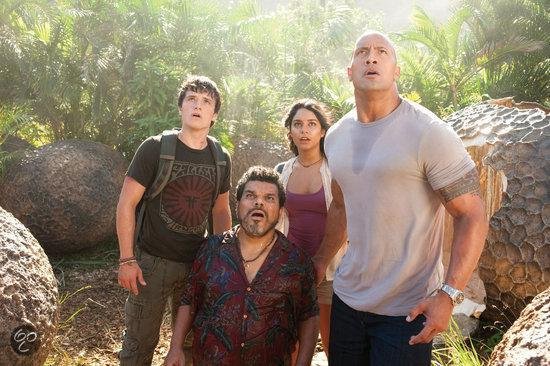 Vier mensen kijken omhoog in een jungle-omgeving: twee mannen, een vrouw en een man in een blouse met papegaaien.
