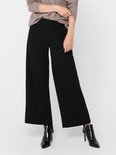 Model met zwarte wijde broek met knoopdetail, gedragen met bruine trui.