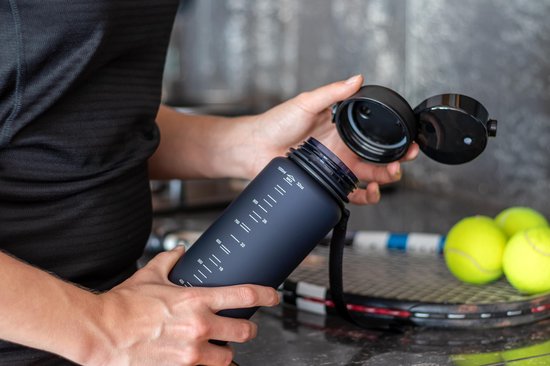 Iemand houdt een donkerblauwe King Mungo drinkfles met volumeaanduiding vast, tennisrackets op achtergrond.