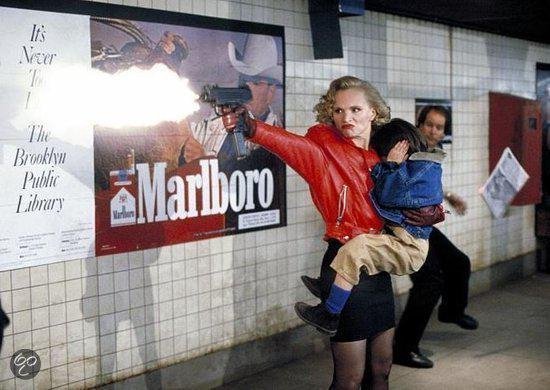 Vrouw in rode jas houdt kind vast en schiet met pistool, met Marlboro-poster op de achtergrond.