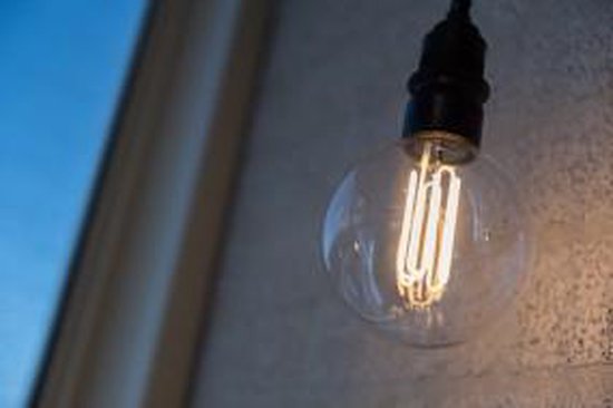 Een gloeilamp met een transparante bol en zichtbare, spiraalvormige filamenten, verlicht.