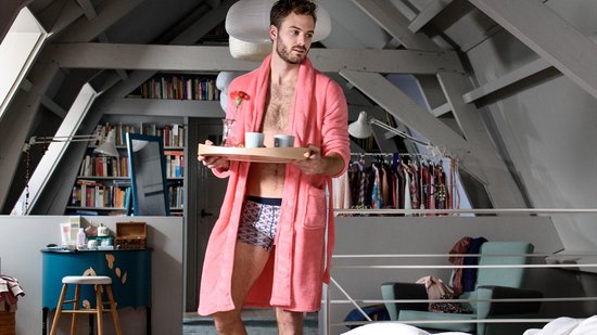 Man in roze badjas en patroononderbroek serveert koffie op een dienblad.