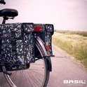Zwarte dubbele fietstas met een vogelprint op een fiets, in een landschap.