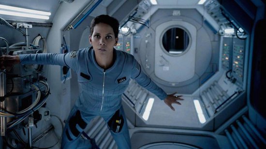 Vrouw met een grijze astronautenpak staand in een gang van een ruimteschip.