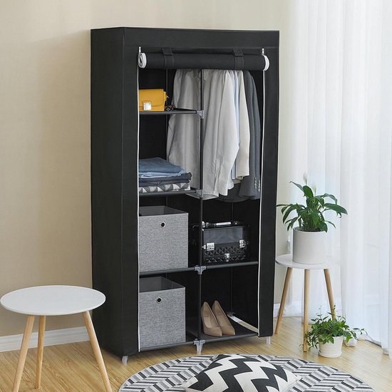 Zwarte stoffen kledingkast met roede en legplanken, gevuld met kleding, dozen en schoenen, in een slaapkamer.