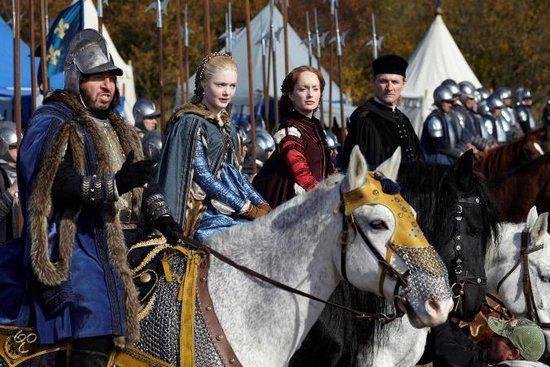 Een vrouw in een blauwe jurk op een wit paard, omringd door soldaten in harnas en mannen te paard.