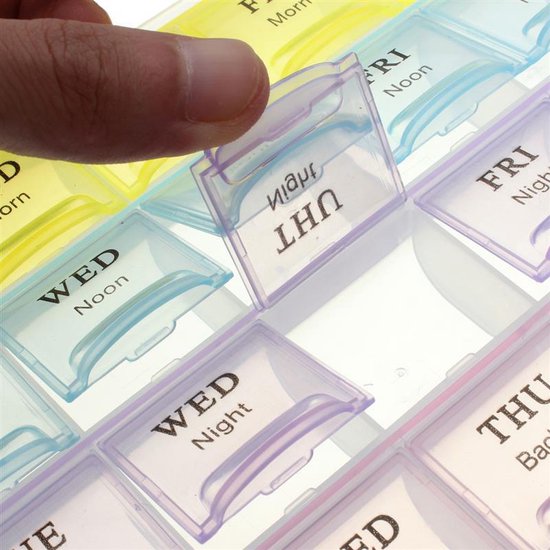 Vinger opent een doorzichtig deksel van een medicijndoosje met de tekst 'WED Noon' erop.