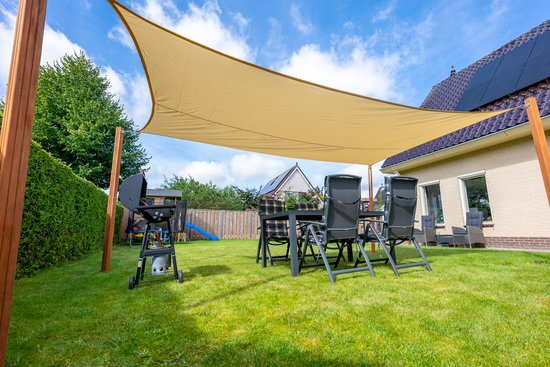 Een beige schaduwdoek is gespannen over een tuin met een eettafel, stoelen en barbecue.