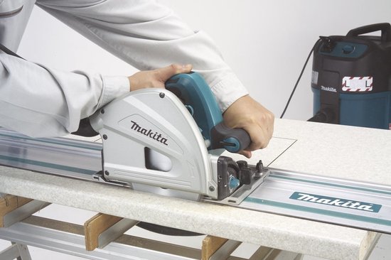 Makita invalcirkelzaag met geleiderail, in gebruik met een stofzuiger op de achtergrond.