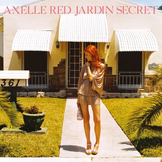 Axelle Red, Jardin Secret. Femme aux cheveux roux se tient sur un chemin devant une maison.