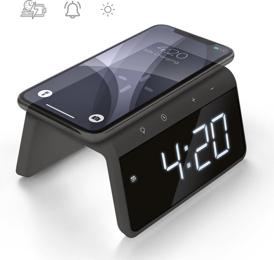 Zwarte digitale wekker met display en een telefoon die draadloos oplaadt.