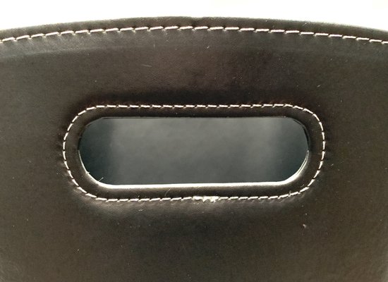 Detail van een handvat van de zwarte kunstleren mand met witte sierstiksels.