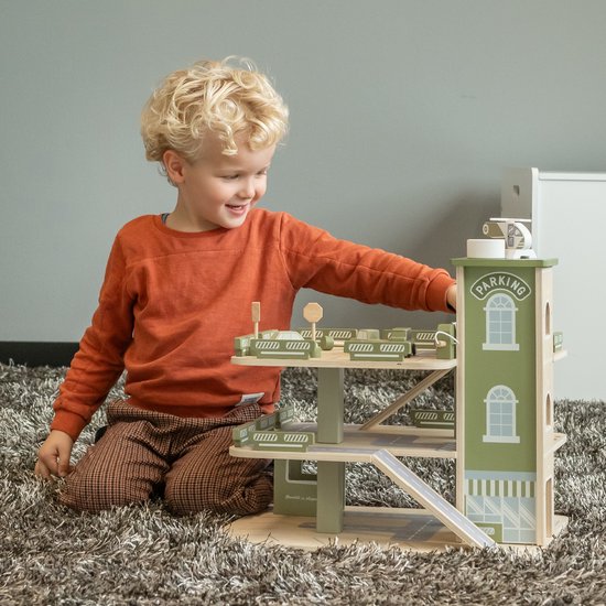Vrolijke jongen met oranje trui speelt met de houten speelgoedparkeergarage in retro groen.
