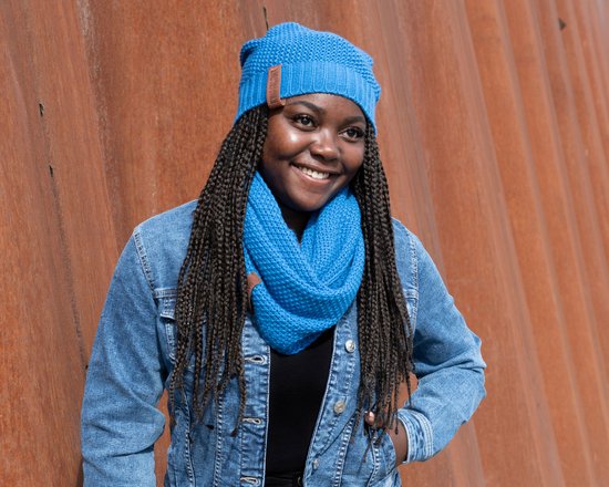 Vrouw met blauwe beanie en sjaal, draagt blauwe denim jas.