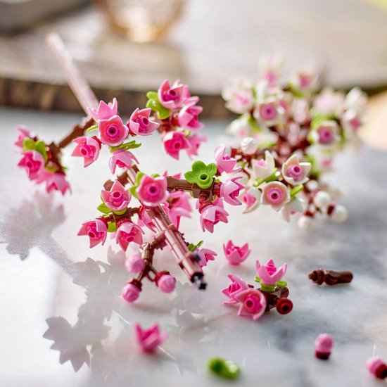 Close-up van LEGO kersenbloesem takken met roze en witte bloemen, en losse onderdelen.