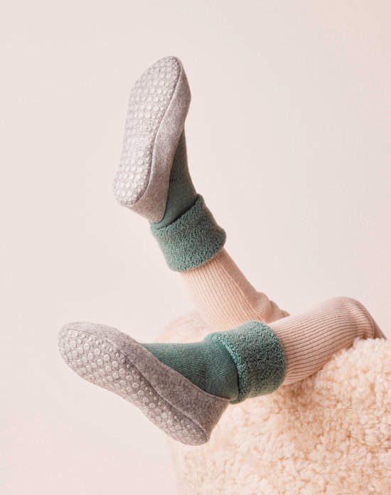 Benen van een pop met beige panty's, lichtgroene sokken met fuzzy rand en grijze antislip pantoffelsokken.