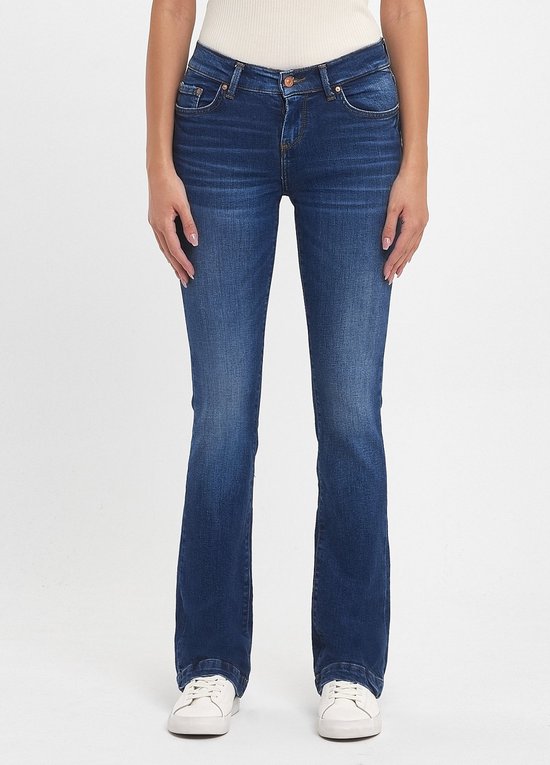 Model in een donkerblauwe flared jeans met subtiele vervagingen en witte sneakers.