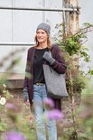 Vrouw met grijze muts en handschoenen draagt een bordeauxrood vest over een zwart shirt en spijkerbroek. Ze draagt een grijze tas.