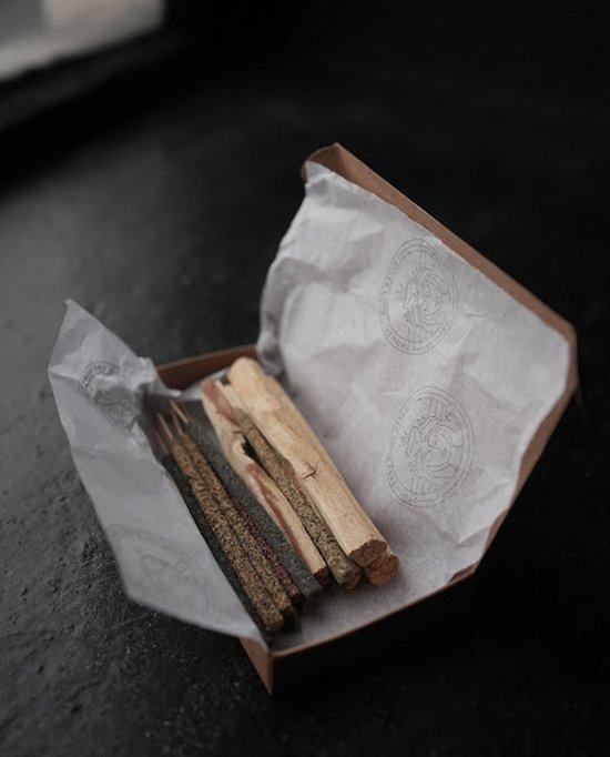 Open doos met een pakje wierookstokjes en enkele stukken palo santo hout, verpakt in wit papier.