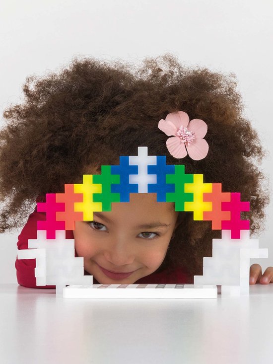 Meisje met krullend haar draagt een regenboog van Plus-Plus bouwstenen op haar hoofd.