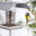 Vogelvoederbak, zilverkleurig dak, transparante silo vol zaadjes, zilverkleurige bak met zaadjes, met een koolmees.