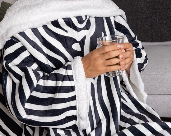 Gedetailleerde opname van de zebra-print deken met mouwen, de witte fleece voering en een hand die een glas vasthoudt.