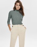 Groene coltrui met lange mouwen, gedragen door een vrouw met een beige broek met hoge taille en knopen.