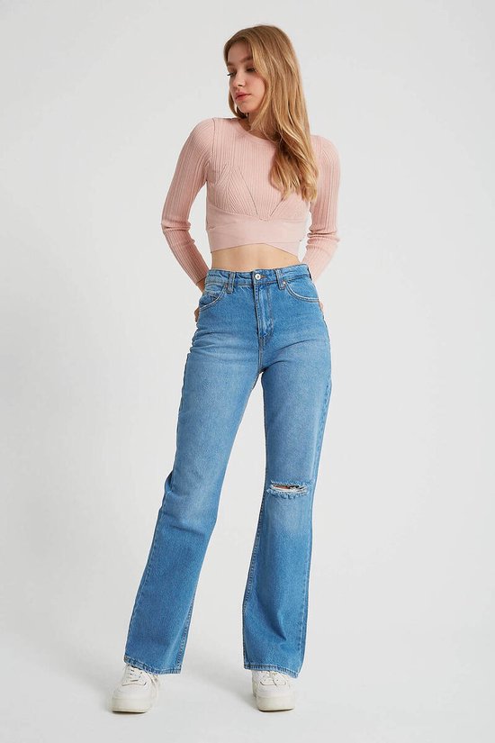 Model draagt lichtblauwe wijde jeans met hoge taille en een gescheurd detail op de knie, met roze crop top.