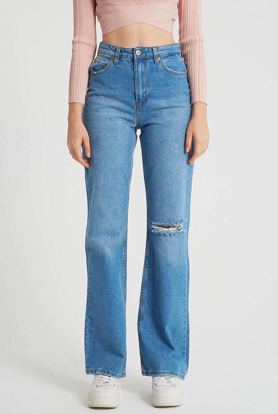 Model draagt een blauwe spijkerbroek met hoge taille en gescheurde knie.