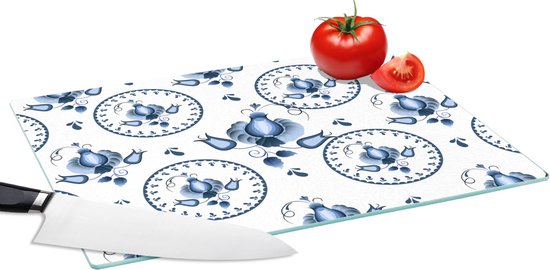 Planche à découper en verre avec décoration florale et tulipes bleues et blanches, avec couteau et tomate.