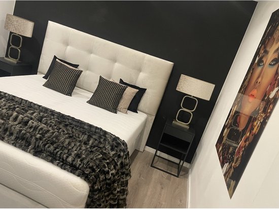 Chique slaapkamer met beige boxspring, vier kussens, sprei, nachtkastje met lamp en een schilderij van een vrouw.