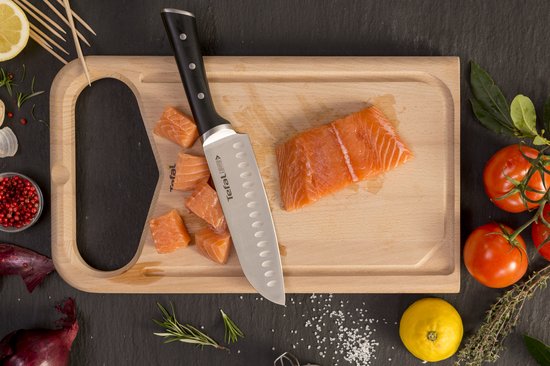 Chef snijdt zalm op houten plank met Tefal santokumes. Naast tomaten, citroen, ui en aardappel.
