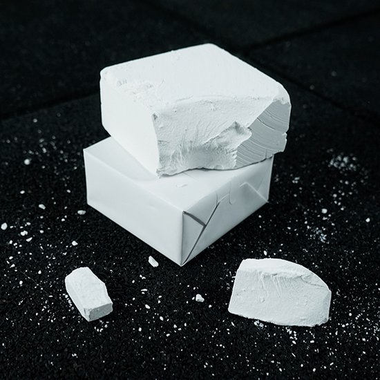Twee witte magnesium blokken, gestapeld, met twee losse stukken en poeder op zwarte ondergrond.