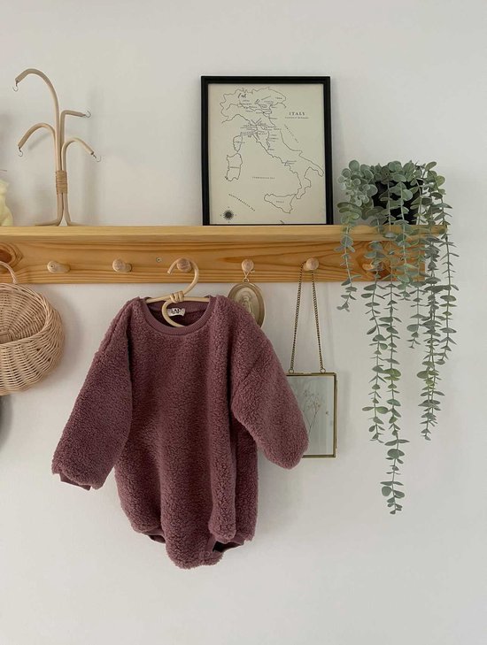 Roze teddy romper met lange mouwen, gedrapeerd over een kledingrek.