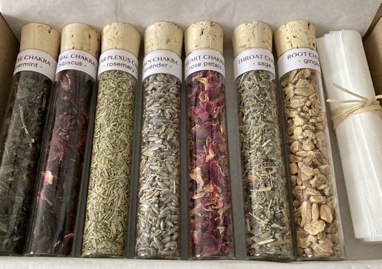 Zeven glazen buisjes met kruiden, geordend in een kartonnen doos. Van links naar rechts: groene thee, hibiscus, rozemarijn, lavendel, rozenblaadjes, salie, gember.