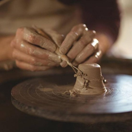 Pottenbakker gebruikt gereedschap om pot van klei te vormen op draaischijf.