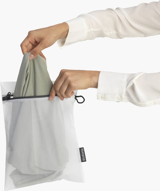 Een hand die een groen kledingstuk in een wit gaaswaszakje stopt.