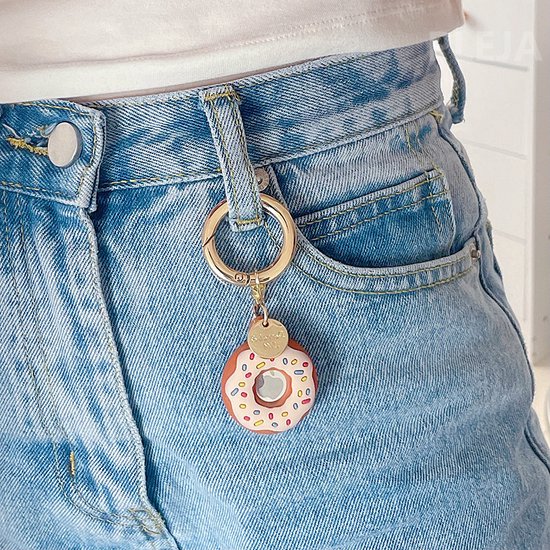 Witte donut sleutelhanger met stippen aan een gouden ring, gedragen aan een spijkerbroek.