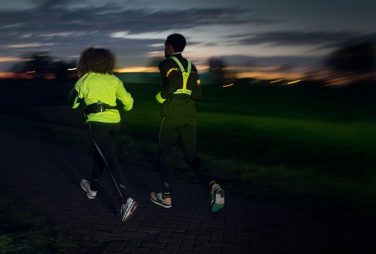 Twee hardlopers in het donker, één met een felgroen vest en de ander met een reflecterend Avento vest met lichtjes.