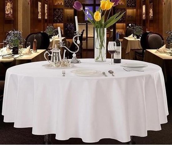 Tafel met wit tafelkleed, gedekte tafel met wijn, glas, kandelaar en bloemen.