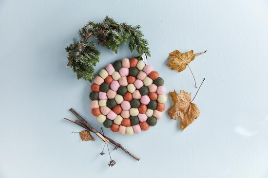 Ronde onderzetter van viltballetjes in kleuren roze, groen, oranje en crème, omringd door herfstdecoratie.