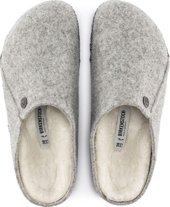 Een paar lichtgrijze vilten Birkenstock pantoffels met een crème kleurige schapenvacht voering, gezien van bovenaf.