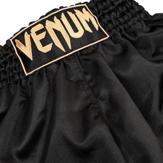 Detailopname van de zwarte elastische tailleband met een goudkleurig geborduurd Venum-label.