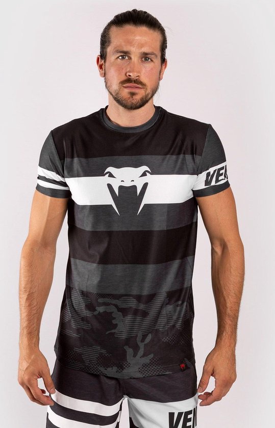 Homme avec queue de cheval portant un t-shirt rayé noir, gris et blanc avec un imprimé camouflage, un logo Venum sur la manche et un grand logo de serpent blanc sur la poitrine.