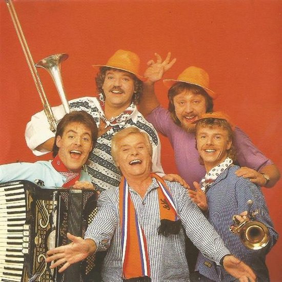 Vijf mannen, sommigen met oranje hoeden en sjaals, lachen en spelen muziek met een accordeon en trompetten.