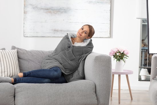 Vrouw zittend op een bank, gehuld in een grijze gewatteerde deken.