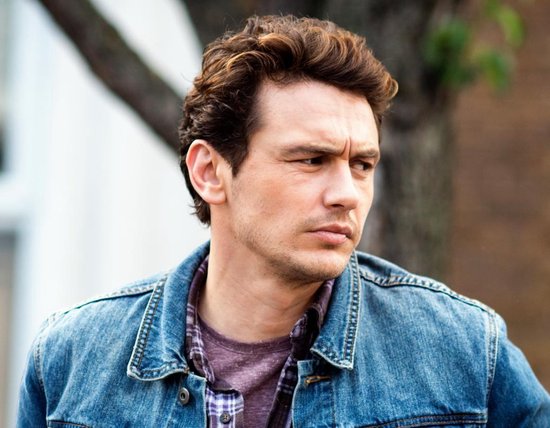 James Franco met donker golvend haar, draagt een denim jas en een geruit shirt.
