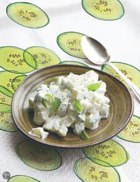 Een bord met een salade van komkommer, yoghurt en munt, met komkommerschijven op de achtergrond.